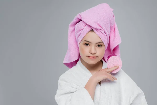 Giovane donna con sindrome di Down in asciugamano e accappatoio tenendo spugna isolata su grigio — Foto stock