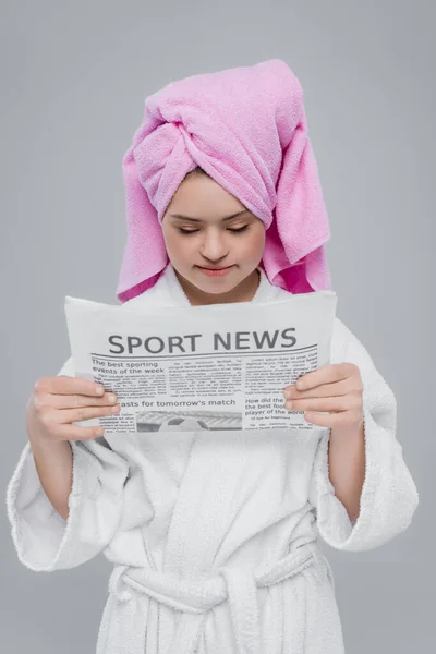 Frau mit Down-Syndrom im Bademantel liest Sportnachrichten isoliert auf grau — Stockfoto