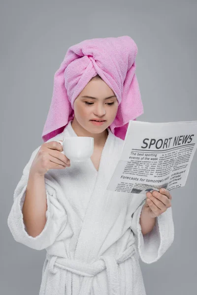 Femme avec le syndrome du duvet en serviette et peignoir lire les nouvelles et tenir la tasse isolée sur gris — Photo de stock