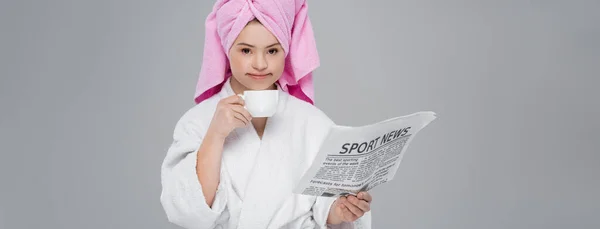 Woman with down syndrome in bathrobe holding sports news and cup isolated on grey, banner — Stock Photo