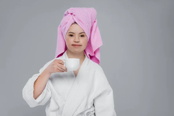 Mujer con síndrome de Down en albornoz y toalla sosteniendo taza aislada en gris - foto de stock