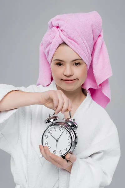 Woman with down syndrome in bathrobe holding alarm clock isolated on grey — Stock Photo