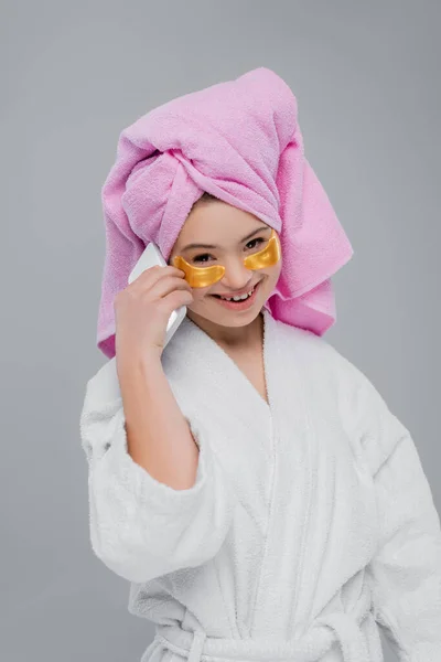 Smiling model with down syndrome in bathrobe and eye patches talking on smartphone isolated on grey — Stock Photo