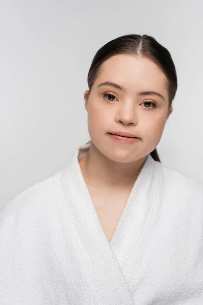 Young woman with down syndrome in bathrobe looking at camera isolated on grey — Stock Photo