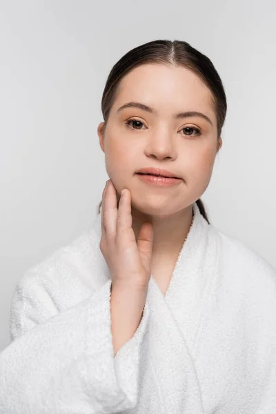 Young woman with down syndrome in bathrobe touching face isolated on grey — Stock Photo