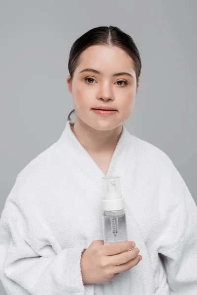 Woman with down syndrome in bathrobe holding cleansing foam isolated on grey — Stock Photo
