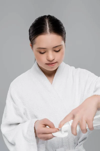 Jeune femme avec syndrome du duvet en peignoir versant de la mousse nettoyante sur du coton isolé sur du gris — Photo de stock