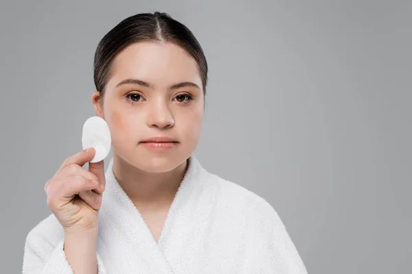 Woman with down syndrome in bathrobe holding cotton pad isolated on grey — Stock Photo