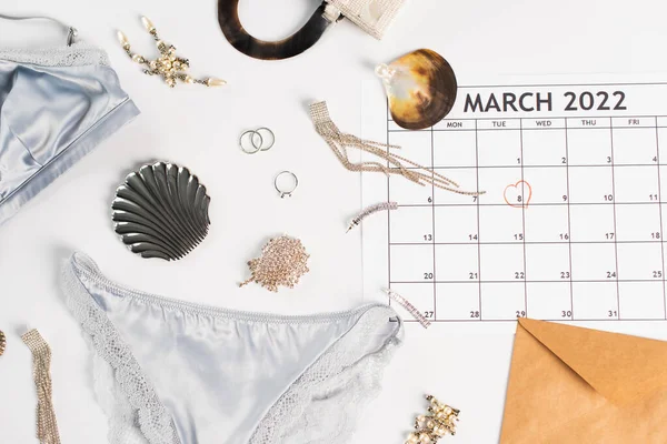 Vista superior de lencería, accesorios y calendario de marzo sobre fondo blanco - foto de stock