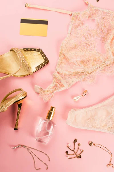 Vista superior del perfume cerca de tacones y lencería sobre fondo rosa - foto de stock