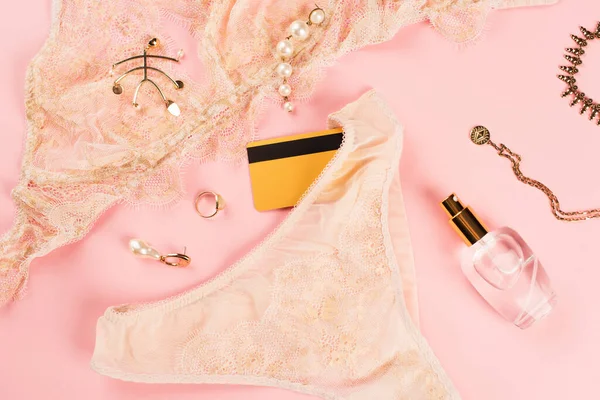 Vista dall'alto della carta di credito vicino lingerie e bottiglia di profumo su sfondo rosa — Foto stock