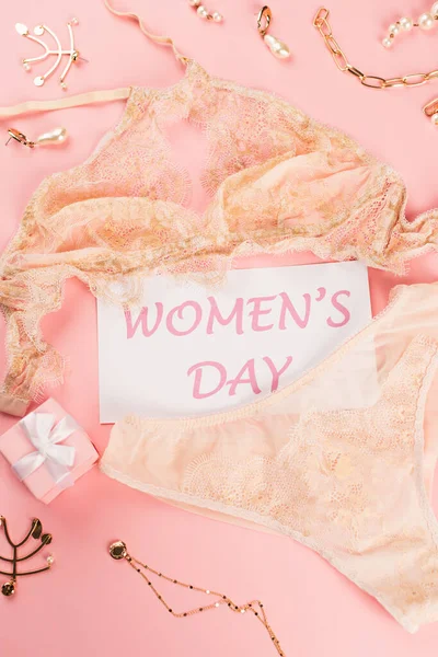 Top view of card with womens day lettering near lingerie, gift box and accessories on pink background — Stock Photo