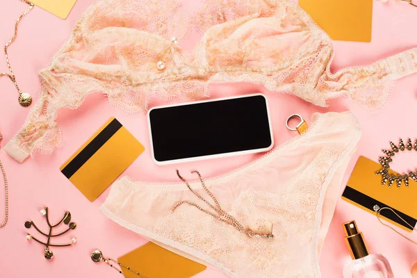 Vista dall'alto dello smartphone con schermo bianco vicino a lingerie, carte di credito e accessori su sfondo rosa — Foto stock