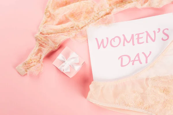 Top view of card with womens day lettering near lingerie and present on pink background — Stock Photo