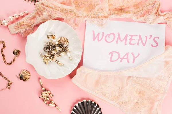 Vista dall'alto della carta con scritte giorno delle donne vicino lingerie di pizzo e accessori su sfondo rosa — Foto stock