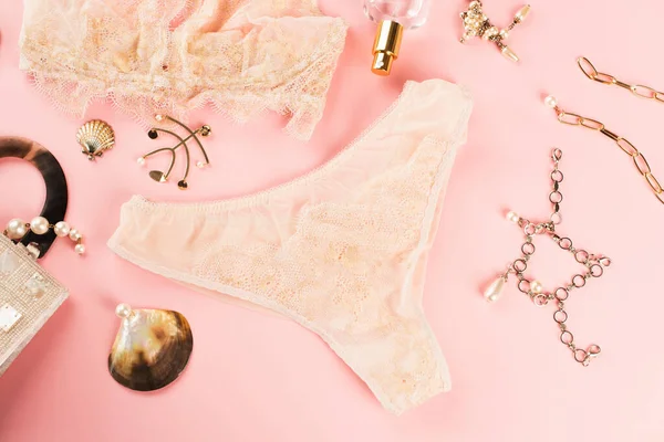 Vue du dessus du parfum près d'accessoires dorés et lingerie pêche sur fond rose — Photo de stock