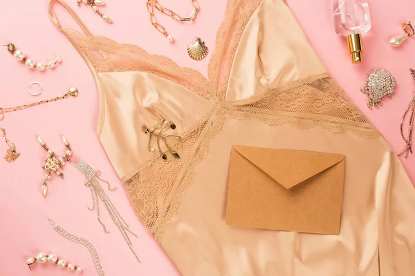 Top view of envelope, golden accessories and camisole on pink background — Stock Photo