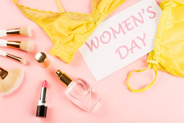 Top view of bra near card with womens day lettering, perfume and cosmetic brushes on pink background — Stock Photo