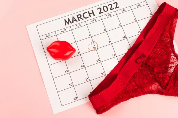Vista superior de las bragas rojas en el calendario de marzo sobre fondo rosa - foto de stock