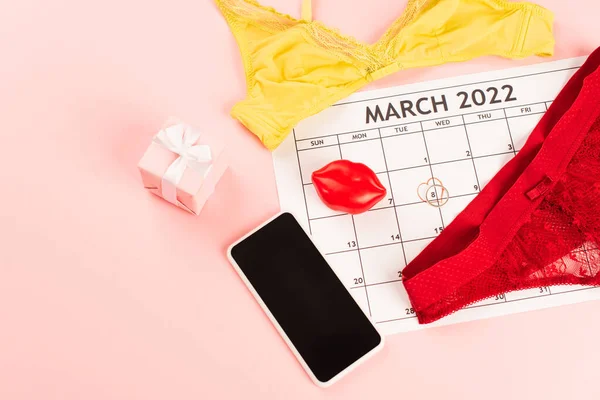 Vista superior do smartphone com tela em branco, calendário de marcha e lingerie no fundo rosa — Fotografia de Stock