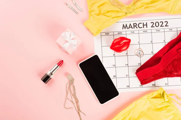 Top view of cellphone near march calendar and lingerie on pink background — Stock Photo