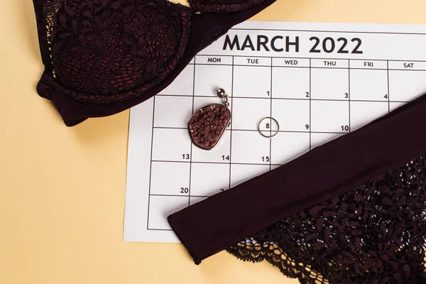 Top view of lingerie on march calendar and accessories on beige background — Stock Photo