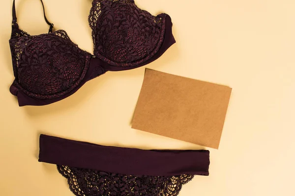 Vue du dessus de lingerie en dentelle noire près de l'enveloppe sur fond beige — Photo de stock