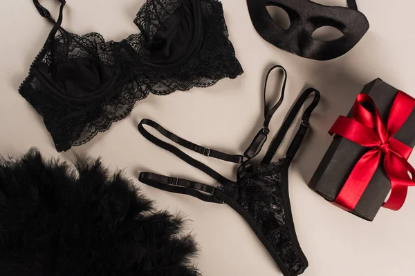 Visão superior de lingerie rendas perto de máscara sexual e presente no fundo cinza — Fotografia de Stock