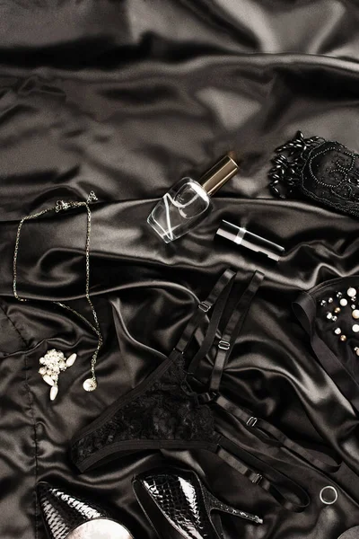 Vista superior de las bragas de encaje cerca de tacones y perfume sobre fondo satinado negro - foto de stock
