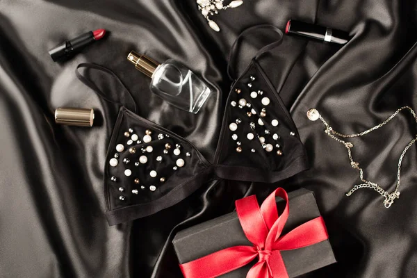 Top view of bra, gift and perfume near lipsticks on black satin background — Stock Photo