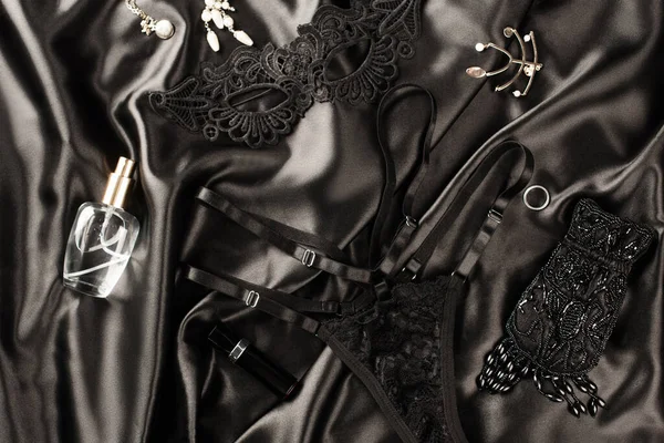 Vue du dessus du masque sexuel près des culottes et du parfum sur fond de satin noir — Photo de stock