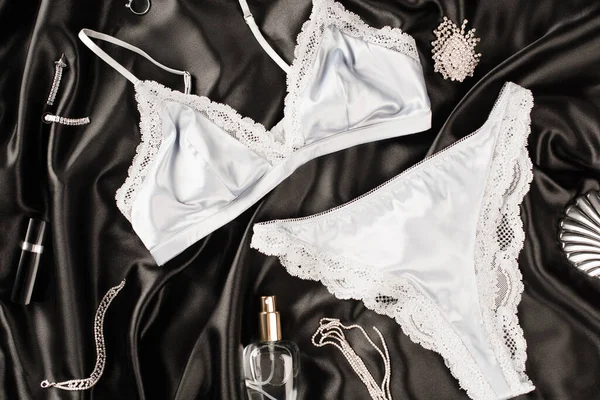 Vista superior de lingerie perto de perfume e acessórios em fundo de cetim preto — Fotografia de Stock