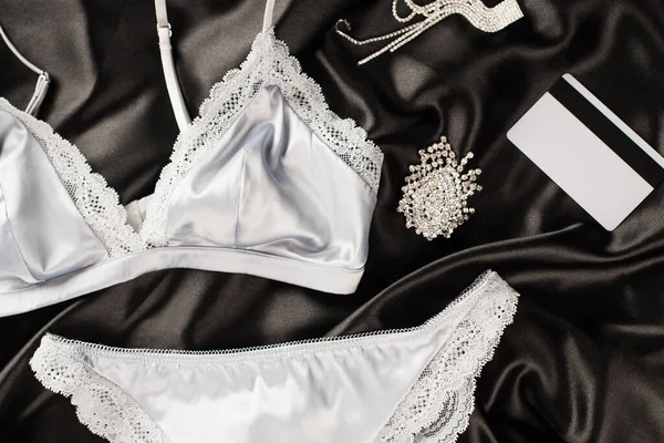 Vue du dessus de lingerie près de carte de crédit et accessoires sur fond satin noir — Photo de stock