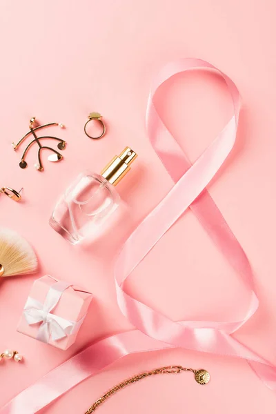 Vue du dessus du ruban en forme de 8 signes près de cadeau, parfum et accessoires sur fond rose — Photo de stock