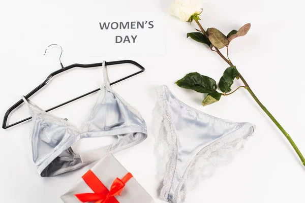 Vue du dessus de la lingerie près de la carte avec lettrage de jour pour femmes, rose et cadeau sur fond blanc — Photo de stock