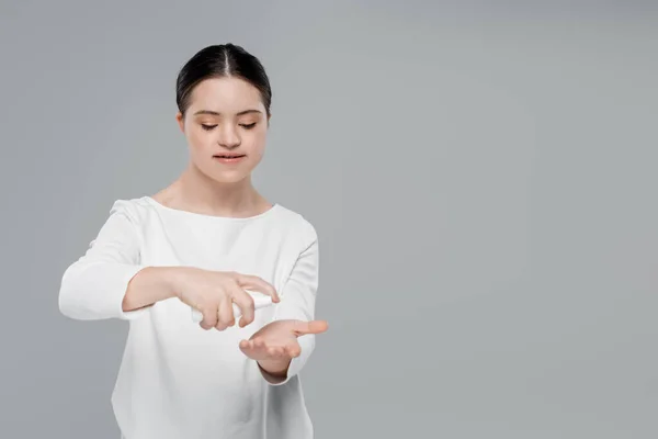 Junge Frau mit Down-Syndrom mit Händedesinfektionsmittel isoliert auf grau — Stockfoto