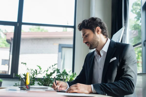 Elegante hombre de negocios en negro blazer escritura en el lugar de trabajo en la oficina - foto de stock