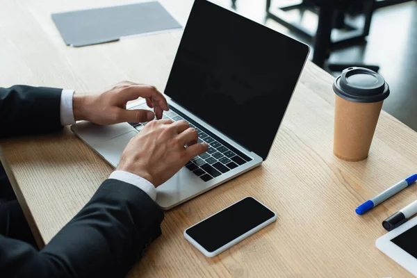 Vista parcial del hombre de negocios escribiendo en el ordenador portátil con pantalla en blanco en el lugar de trabajo en la oficina - foto de stock