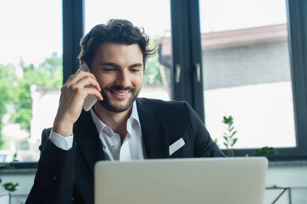 Hombre de negocios elegante y feliz hablando en el teléfono móvil en la oficina - foto de stock