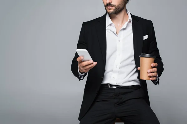 Vista parcial del hombre elegante con bebida para llevar y teléfono móvil sentado aislado en gris - foto de stock