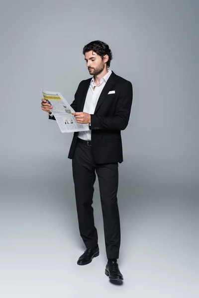 Full length view of man in black suit reading newspaper on grey — Stock Photo