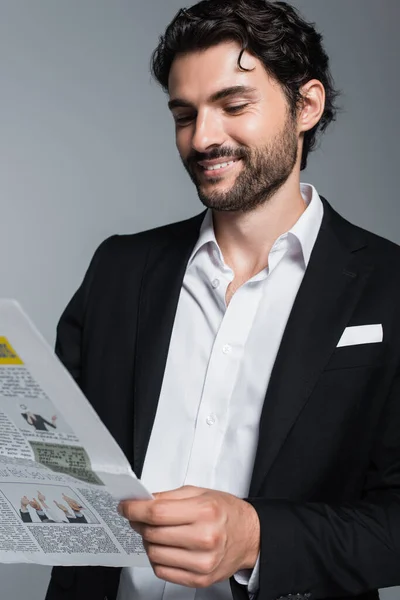 Щаслива брюнетка бізнесмен в чорному блейзер читання газеті ізольовані на сірому — стокове фото
