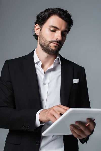 Homme d'affaires en blazer noir et chemise blanche en utilisant une tablette numérique isolée sur gris — Photo de stock