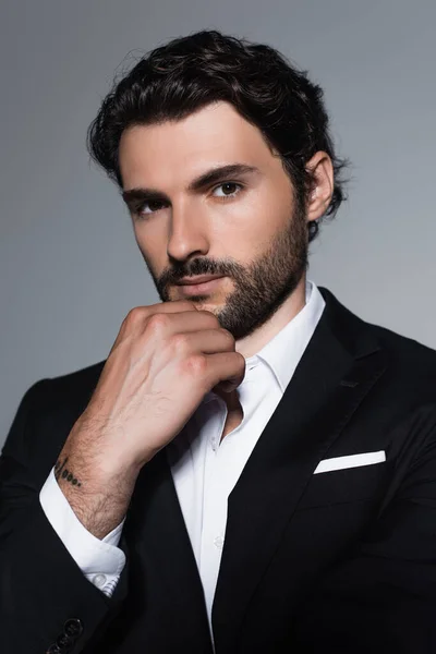 Elegant brunette man looking at camera while holding hand near face isolated on grey — Stock Photo