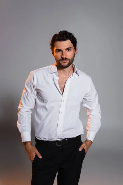 Stylish man in white shirt standing with hands in pockets of black trousers on grey — Stock Photo