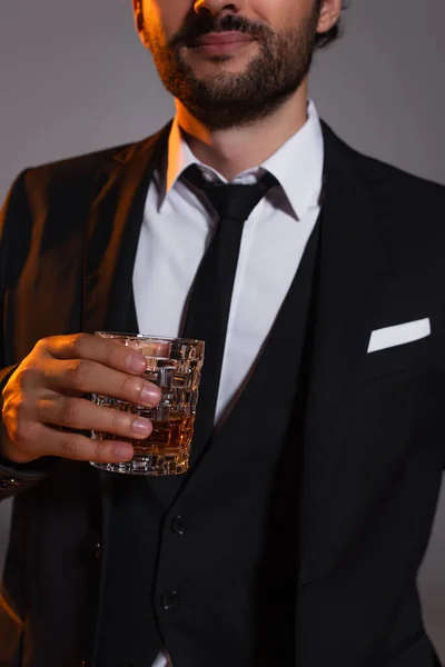 Vue recadrée de l'homme dans une élégante tenue formelle tenant verre de whisky isolé sur gris — Photo de stock