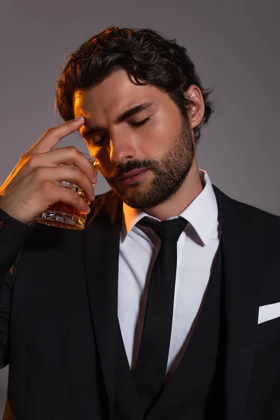 Hombre de negocios cansado con los ojos cerrados sosteniendo vaso de whisky aislado en gris - foto de stock