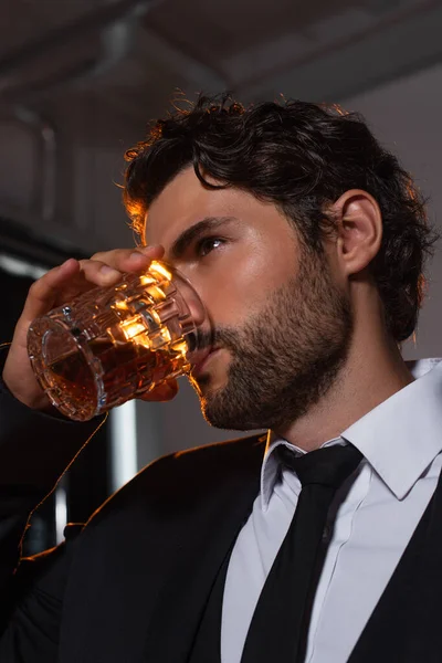 Elegante uomo barbuto bere whisky su sfondo grigio — Foto stock