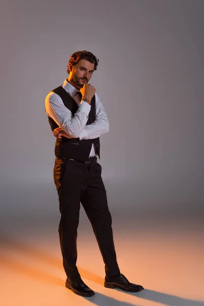 Full length view of elegant brunette man looking at camera while standing on grey background with light — Stock Photo