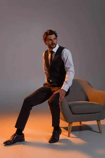 Full length view of elegant businessman looking away near armchair on grey background with light — Stock Photo